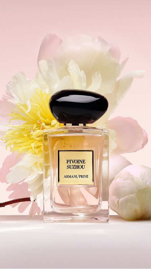 Bottle of Armani/Prive Pivoine Suzhou against a light pink background with floral ingredients.