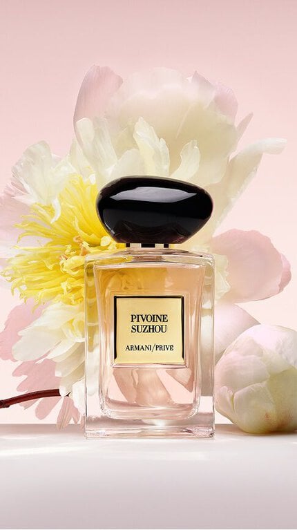Bottle of Armani/Prive Pivoine Suzhou against a light pink background with floral ingredients.