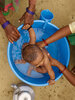 The arms of two people washing a baby boy in a water-filled blue tub.
