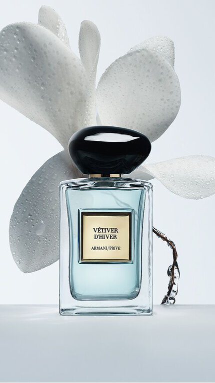 Bottle of Armani/Prive Vetiver D’Hiver against a light blue with floral ingredients.