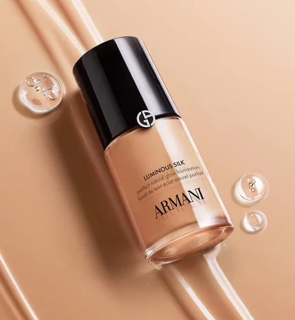 Image Armani Luminous Silk foundation bottle in beige packaging surrounded by dewdrops on a golden beige background.