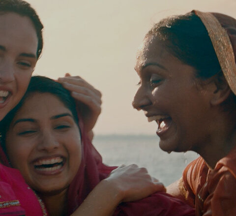 Three girls laughing and hugging on the beach