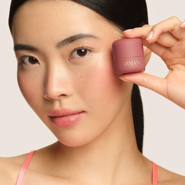 Model holding plum Armani Beauty Dolci Blush, a cream-to-powder blush with a natural finish.