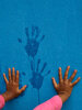 Two hands of a child up against a blue wall with image of handprints in between their hands