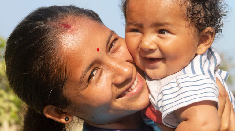 A smiling woman holds a happy infant