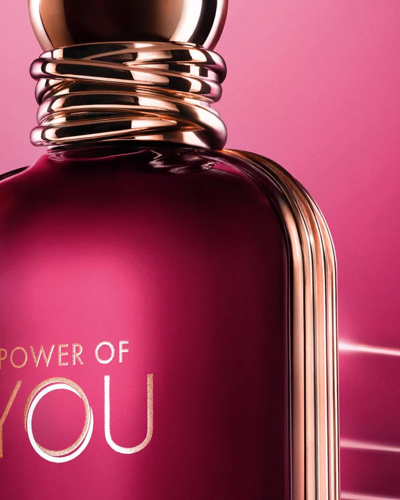 Close-up of the ARMANI POWER OF YOU perfume bottle, glowing in radiant ruby tones with sleek gold accents.