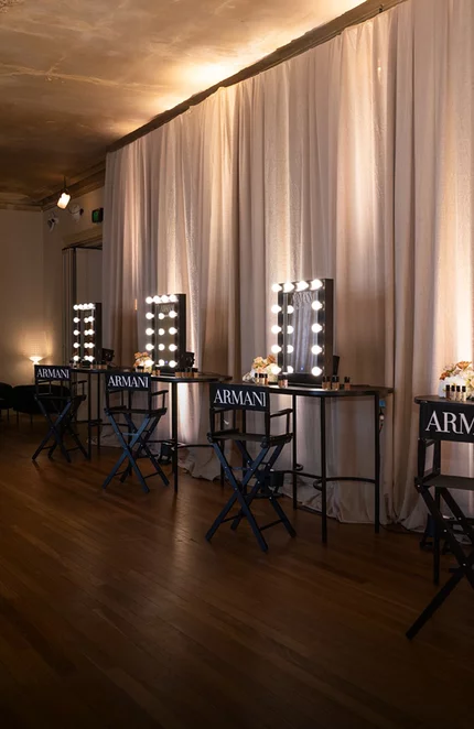 Elegant Armani Beauty event space featuring vanity mirrors with warm bulb lighting and minimalist black stools.