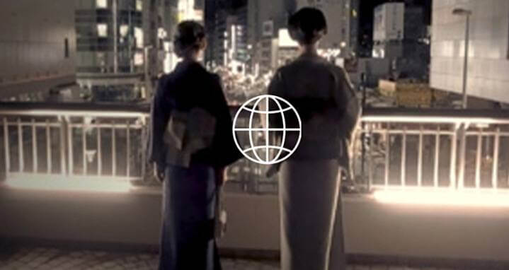 Black and white of the backs of two women with long robes on balcony as they look out to lighted city