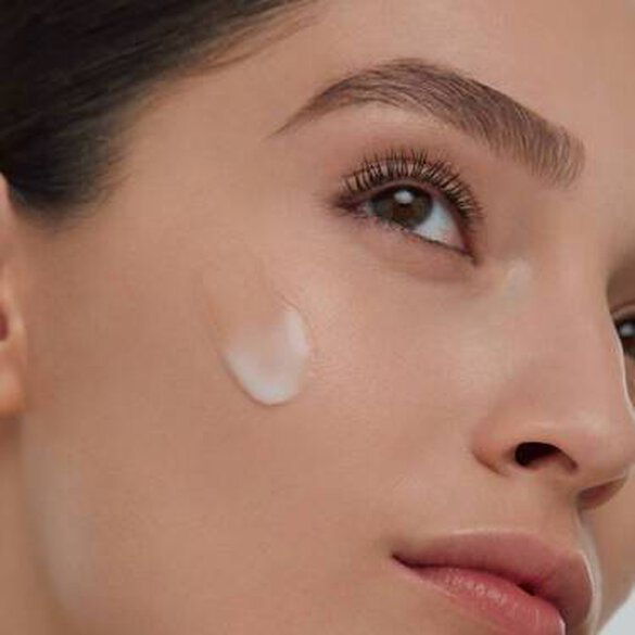 video image of woman that starts as extreme closeup of side of cheek then revealing her head and bare shoulders with minimal makeup looking ahead